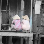 Two women gossiping by the Mekong River in their conical hats
