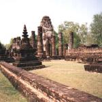 Part of an ancient building, with a statue of Buddha in the background. This buildings surround the entrace of an ancient Wat.