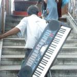 A blind keyboard player lugs his instrument up the stairs.
